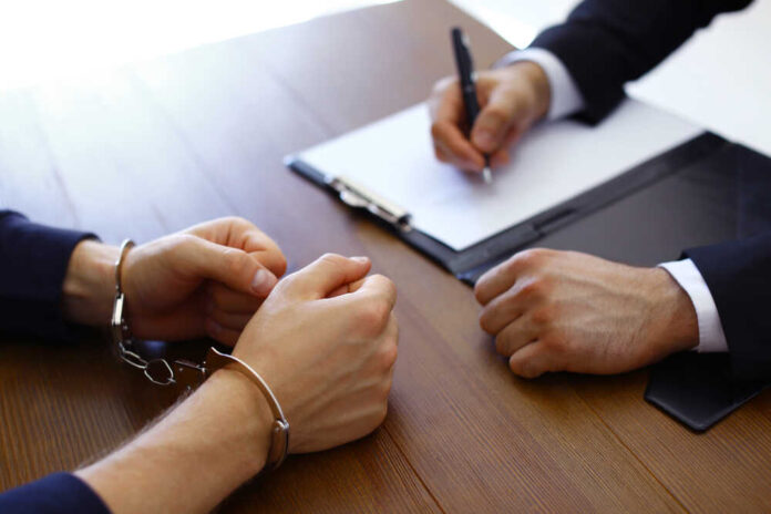 Police,Officer,Interrogating,Criminal,In,Handcuffs,At,Desk,Indoors