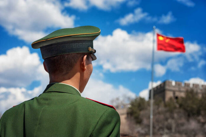 shutterstock_139621247.jpg Soldier in a green military uniform facing the Great Wall of China with the Chinese flag in the background