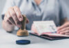 A hand holding a wooden stamp above a passport on a table