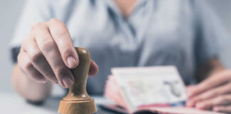 A hand holding a wooden stamp above a passport on a table