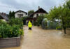 Person in yellow jacket wading through flooded residential area.