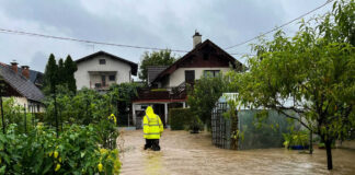 Person in yellow jacket wading through flooded residential area.