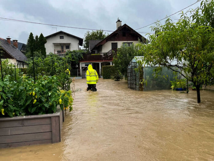 Person in yellow jacket wading through flooded residential area.