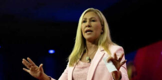 Woman speaking on stage wearing pink blazer