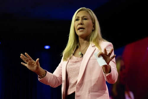 Woman speaking on stage wearing pink blazer