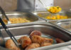 Buffet with sausages and yellow rice in trays.
