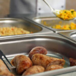 London’s £5 Buffet Shocker: Too Good to Be True? Buffet with sausages and yellow rice in trays.