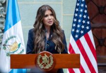 Noem’s Immigration Agenda – Under the Microscope A woman speaking at a podium with flags in the background