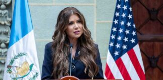 A woman speaking at a podium with flags in the background