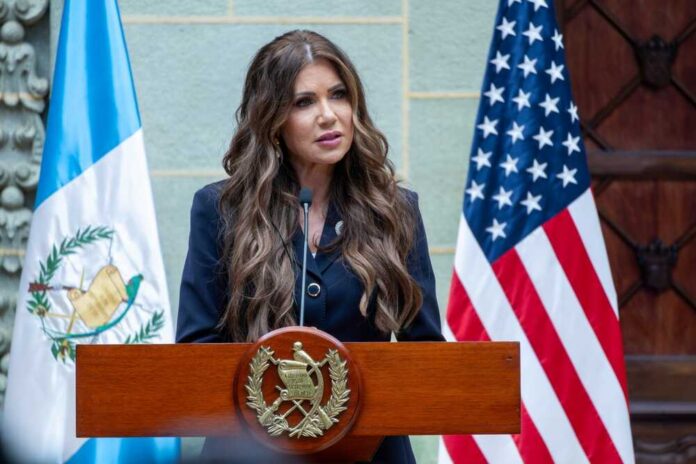 A woman speaking at a podium with flags in the background