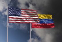 Flags of the United States and Venezuela waving against a cloudy sky