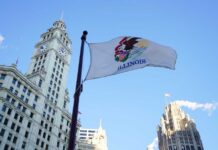 Illinois state flag waving in front of historic buildings against a blue sky