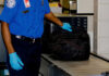 Security worker inspecting black bag on conveyor belt