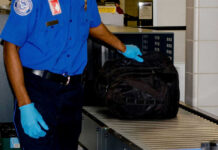 Security worker inspecting black bag on conveyor belt