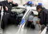 Police officers detaining person in back of patrol car.