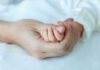 Adult hand holding a babys hand tightly