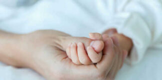 Adult hand holding a babys hand tightly