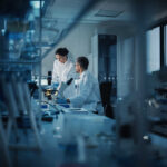 Two scientists working in a laboratory with a microscope and computer screens