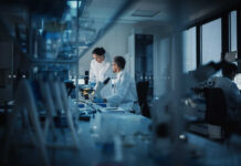 Two scientists working in a laboratory with a microscope and computer screens