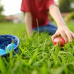 Skims Co-Founder SLAMMED for Parenting Stance Child reaching for a red Easter egg on the grass
