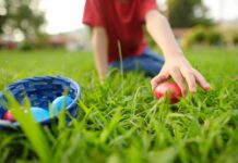 Child reaching for a red Easter egg on the grass