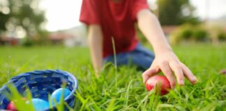 Child reaching for a red Easter egg on the grass