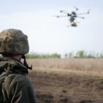A soldier observing a drone flying over a field
