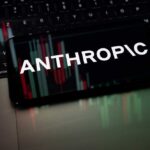 Smartphone displaying the word 'ANTHROPIC' over a background of financial graphs
