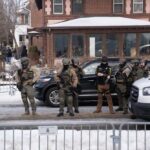 Anti-ICE Mob ASSAULTS Reporter — DOJ Steps In Law enforcement officers in tactical gear at a crime scene in winter