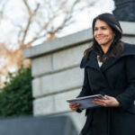 Person holding papers outdoors in a coat smiling