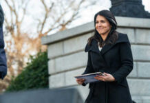 Tensions Rise: Rumors of Gabbard’s Ouster Swirl Person holding papers outdoors in a coat smiling