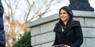 Person holding papers outdoors in a coat smiling