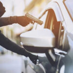 Person in hoodie aiming gun at car occupant