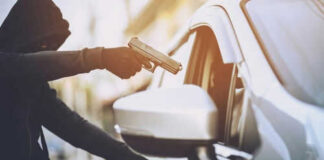 Person in hoodie aiming gun at car occupant