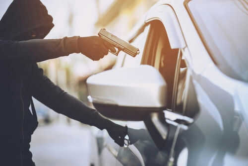 Person in hoodie aiming gun at car occupant