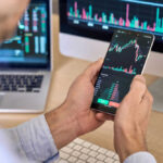 Shock Charges! Wall Street Icon Accused of Double-Dealing Person checking stock market graphs on phone and monitors.