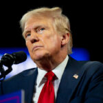 Media Historian SLAMS Trump-Colbert Feud man in suit and red tie speaking at a microphone