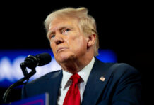 Media Historian SLAMS Trump-Colbert Feud man in suit and red tie speaking at a microphone