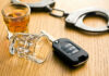 Drunk Driver’s Sidewalk Rampage Caught on Camera Car key glass and handcuffs on wooden table
