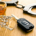 Car key glass and handcuffs on wooden table