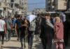 Crowd walking through a dusty street between damaged buildings