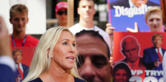 Woman speaking at outdoor event with protest signs in background
