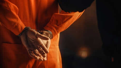 Person in orange jumpsuit with hands cuffed behind back