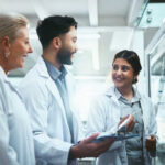 Three scientists discussing notes in laboratory setting