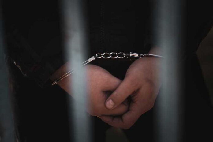 shutterstock_2400784199.jpg Close-up of handcuffed hands behind bars