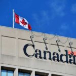 Canadian flag waving atop a building with the word 'Canada' displayed