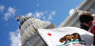 California state flag held up in front of a government building under a blue sky