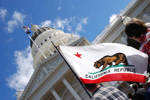 shutterstock_642199051.jpg California state flag held up in front of a government building under a blue sky