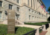 Government building with flags and informational sign outside.