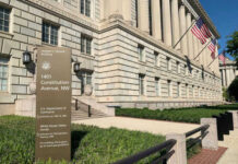 Government building with flags and informational sign outside.